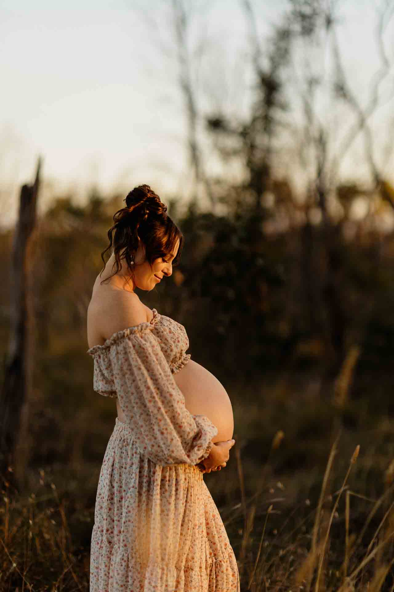 A pregnant mother wearing a 2 piece floral set looking at her pregnant belly at a maternity session in Adelaide.