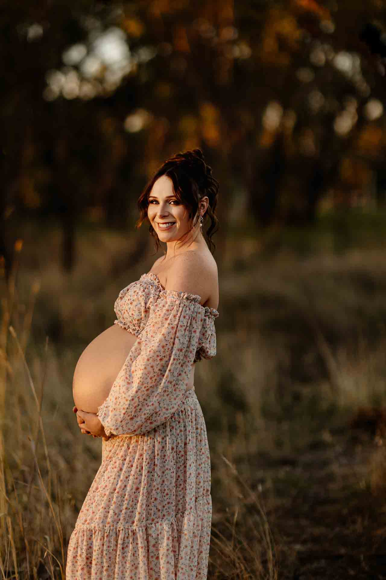 A pregnant mother wearing a 2 piece floral set smiling at a maternity session in Adelaide.