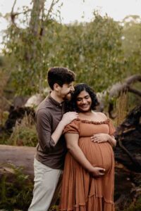 A pregnant mother wearing a rust dress laughing with her partner at a maternity session in the Adelaide Hills.