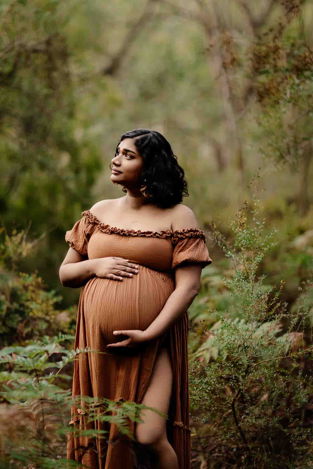 A pregnant mother wearing a rust dress holding her pregnant belly at a maternity session in the Adelaide Hills.