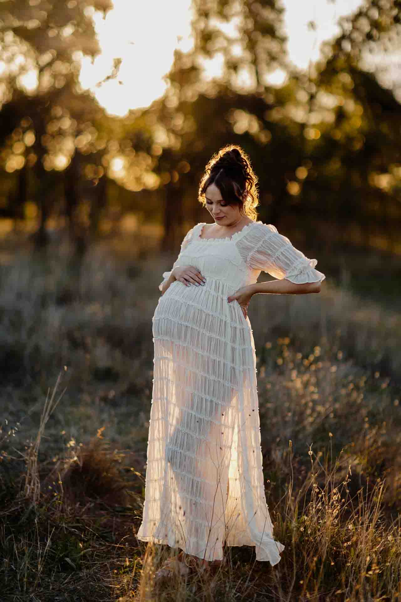 A pregnant mother in a back lit white dress smiling at a maternity session in Adelaide.