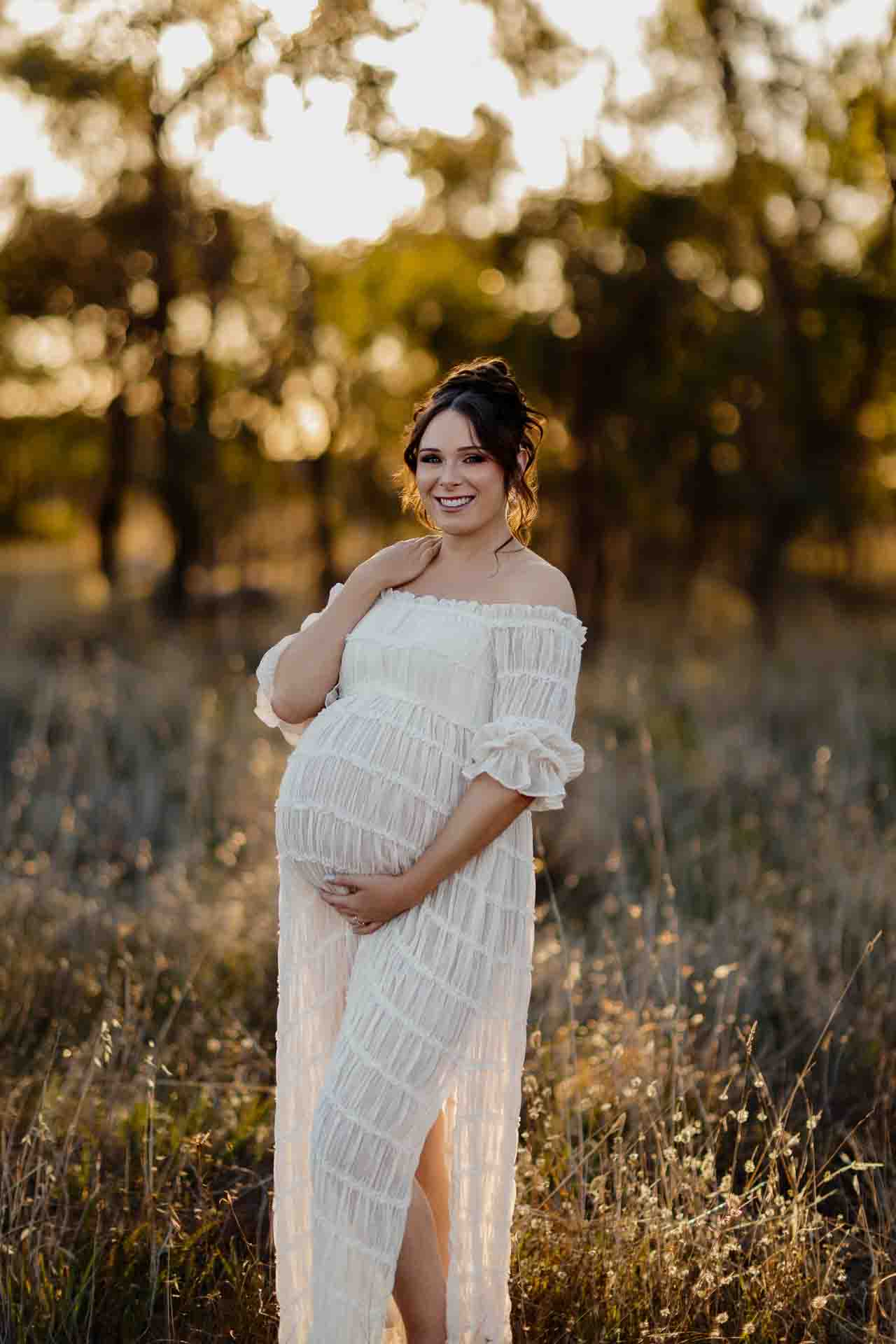 A pregnant mother in a white dress smiling at a maternity session in Adelaide.