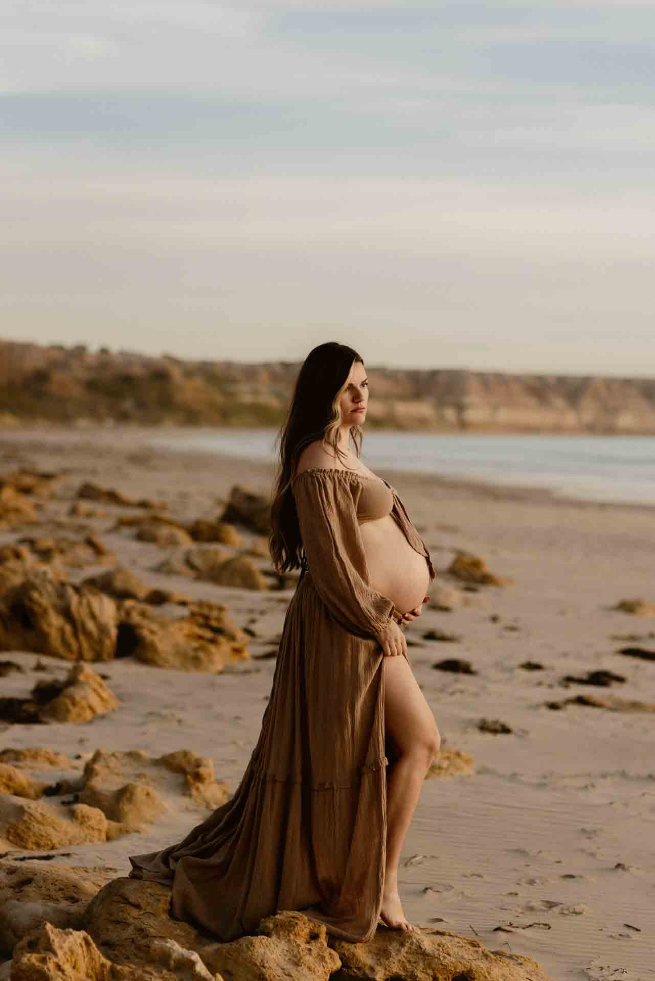 Pregnant woman standing on the beach overlooking the ocean during a maternity session
