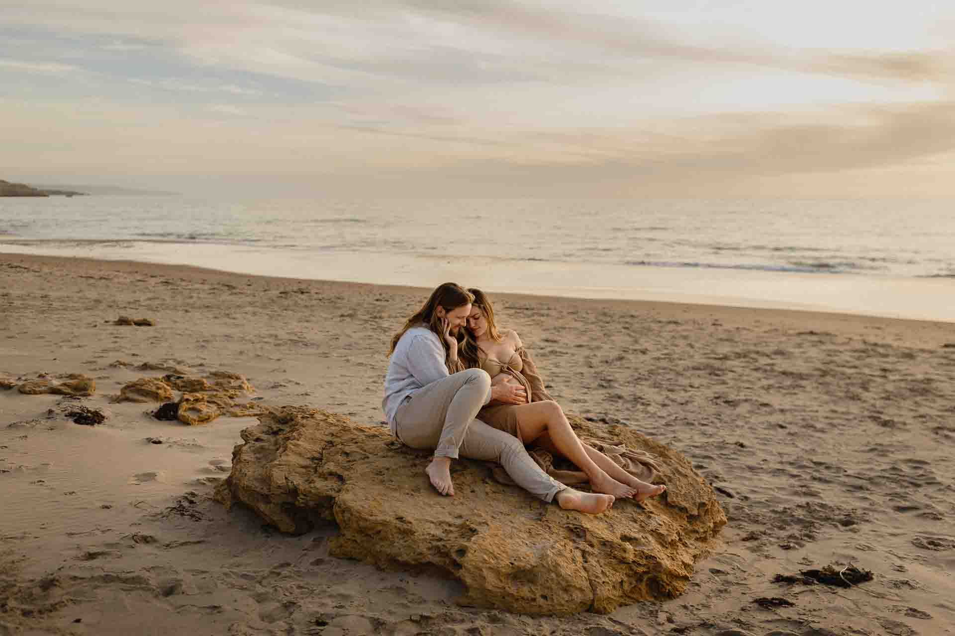 Couple sitting together on rocks overlooking the ocean during a maternity session