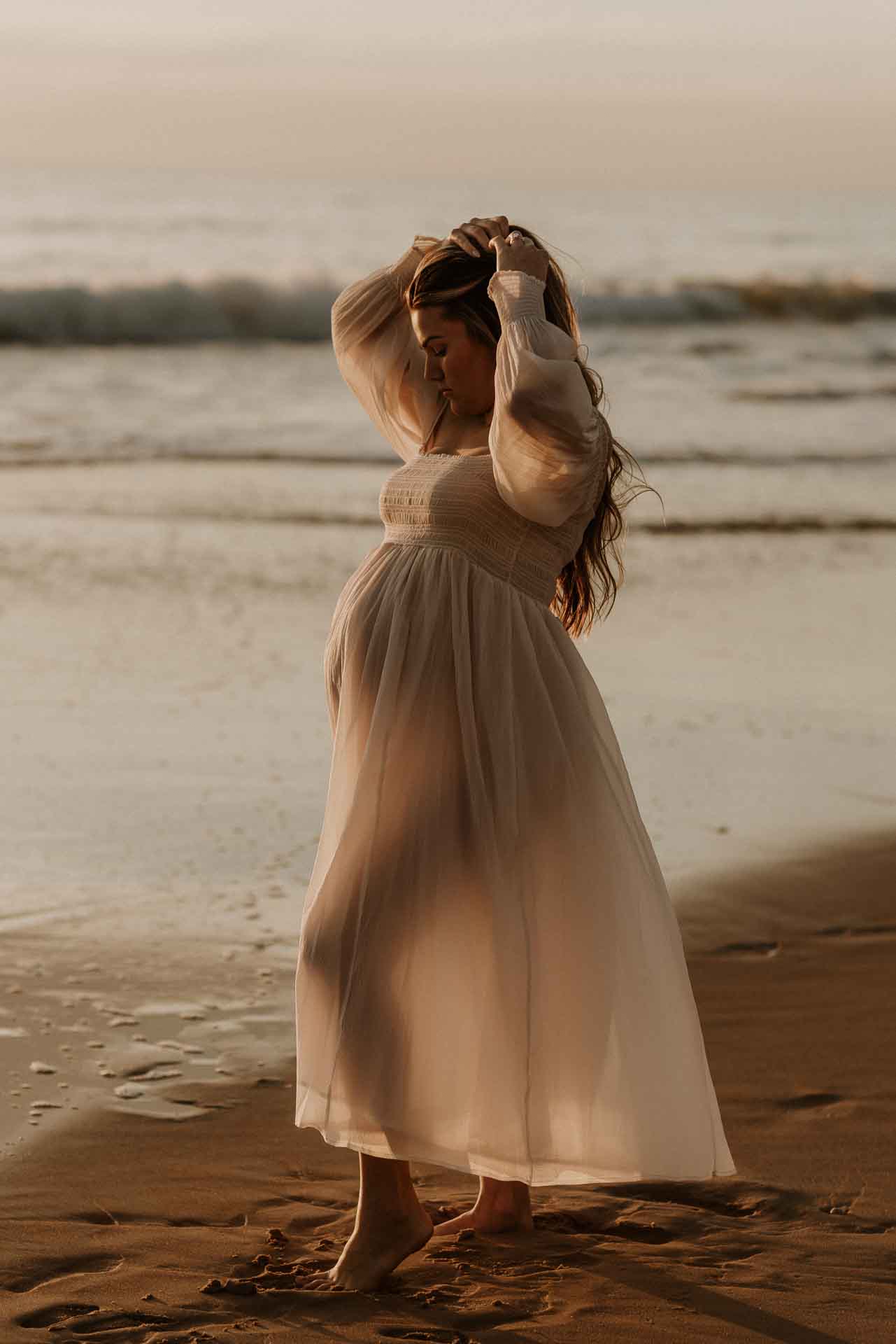 Pregnant woman standing on the beach in a flowing white dress