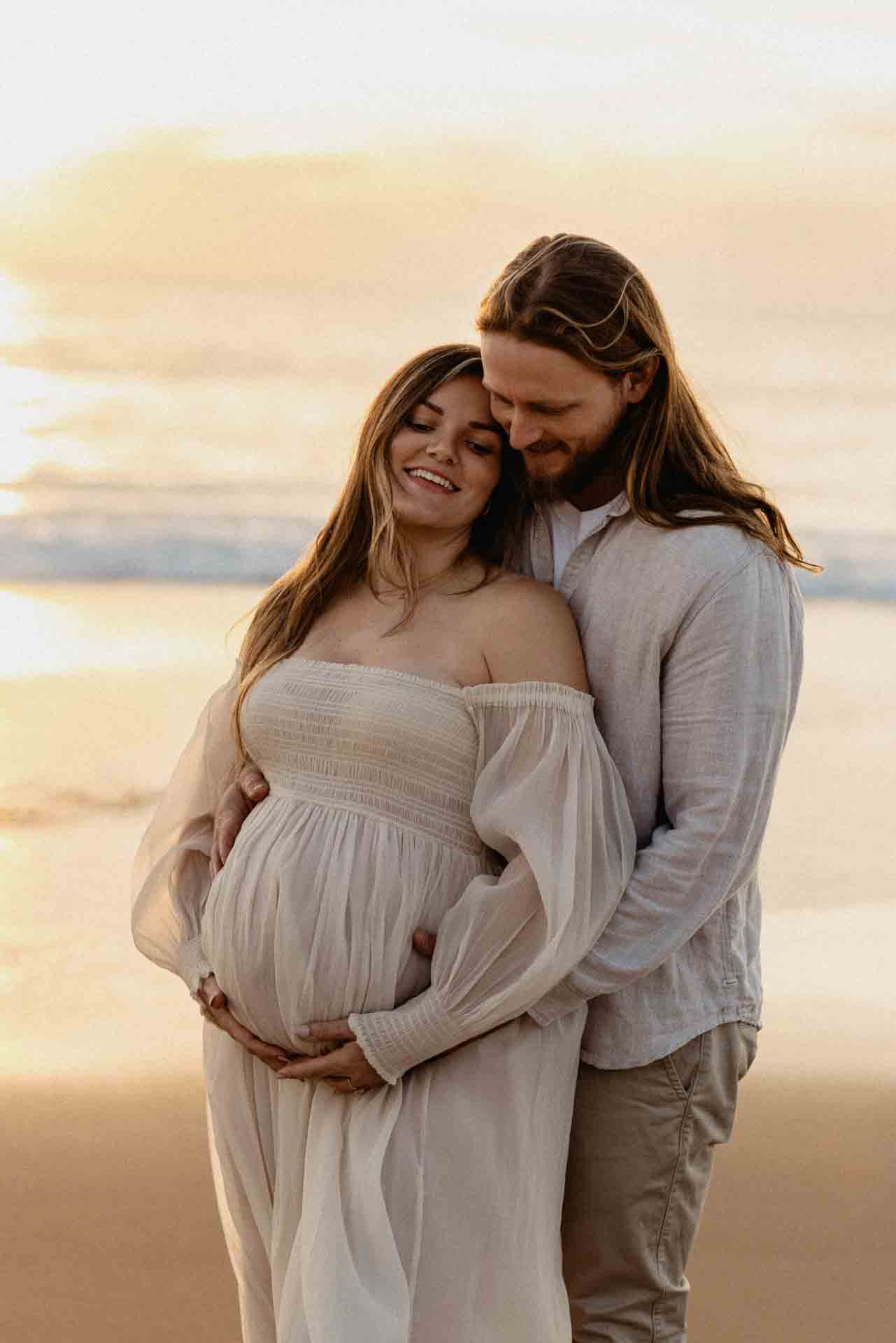 Couple embracing on the beach during a maternity photography session