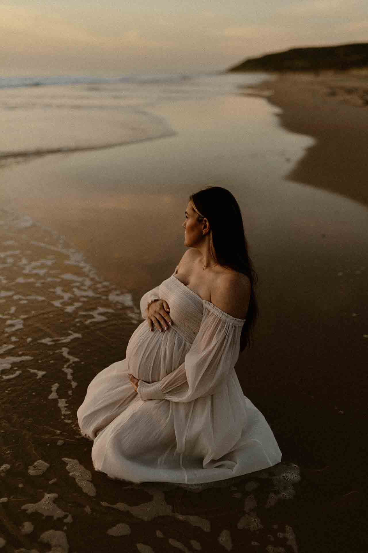 Pregnant woman kneeling in shallow water beside the beach