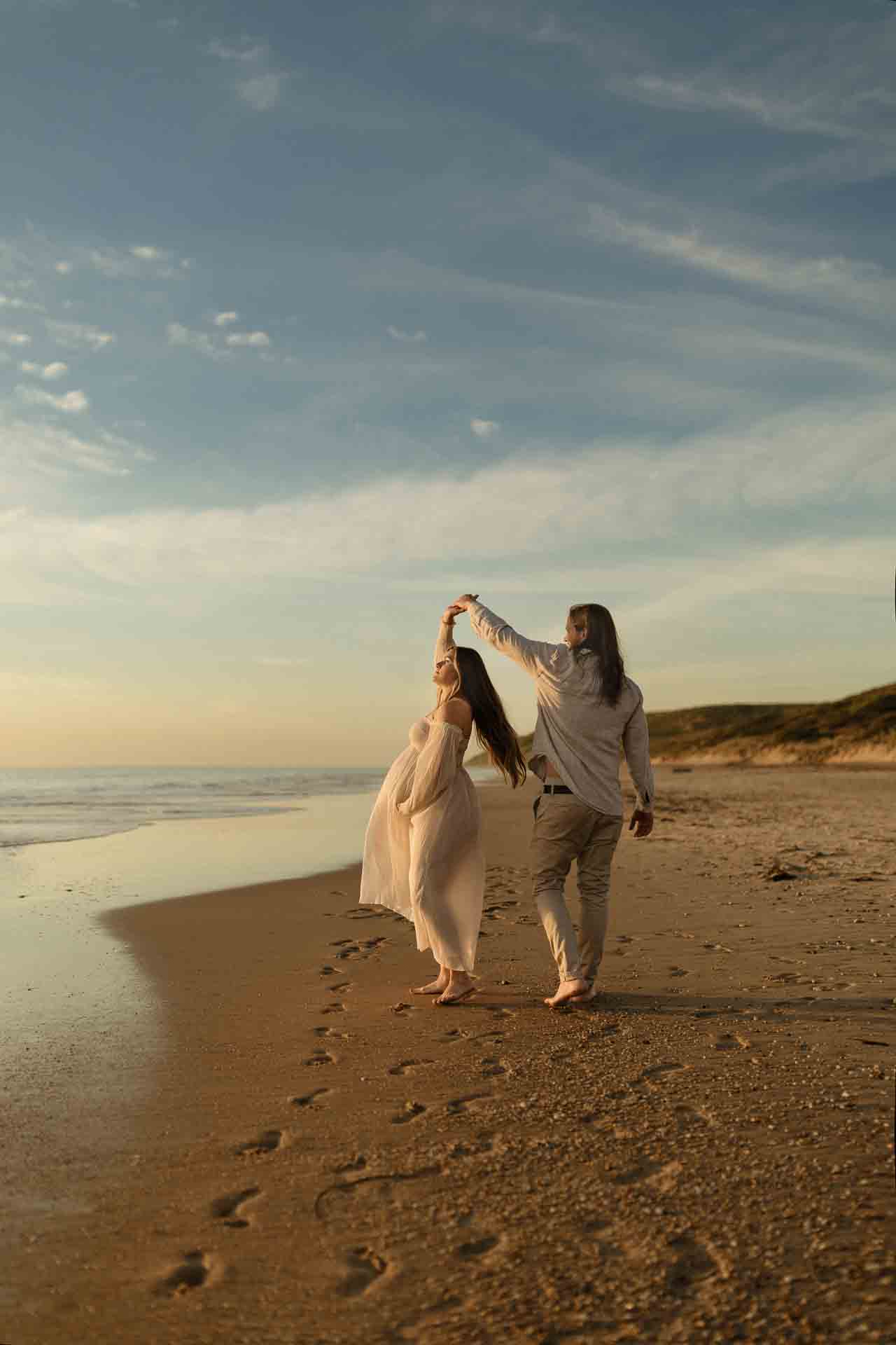 Couple walking together beside the ocean during a beach maternity session