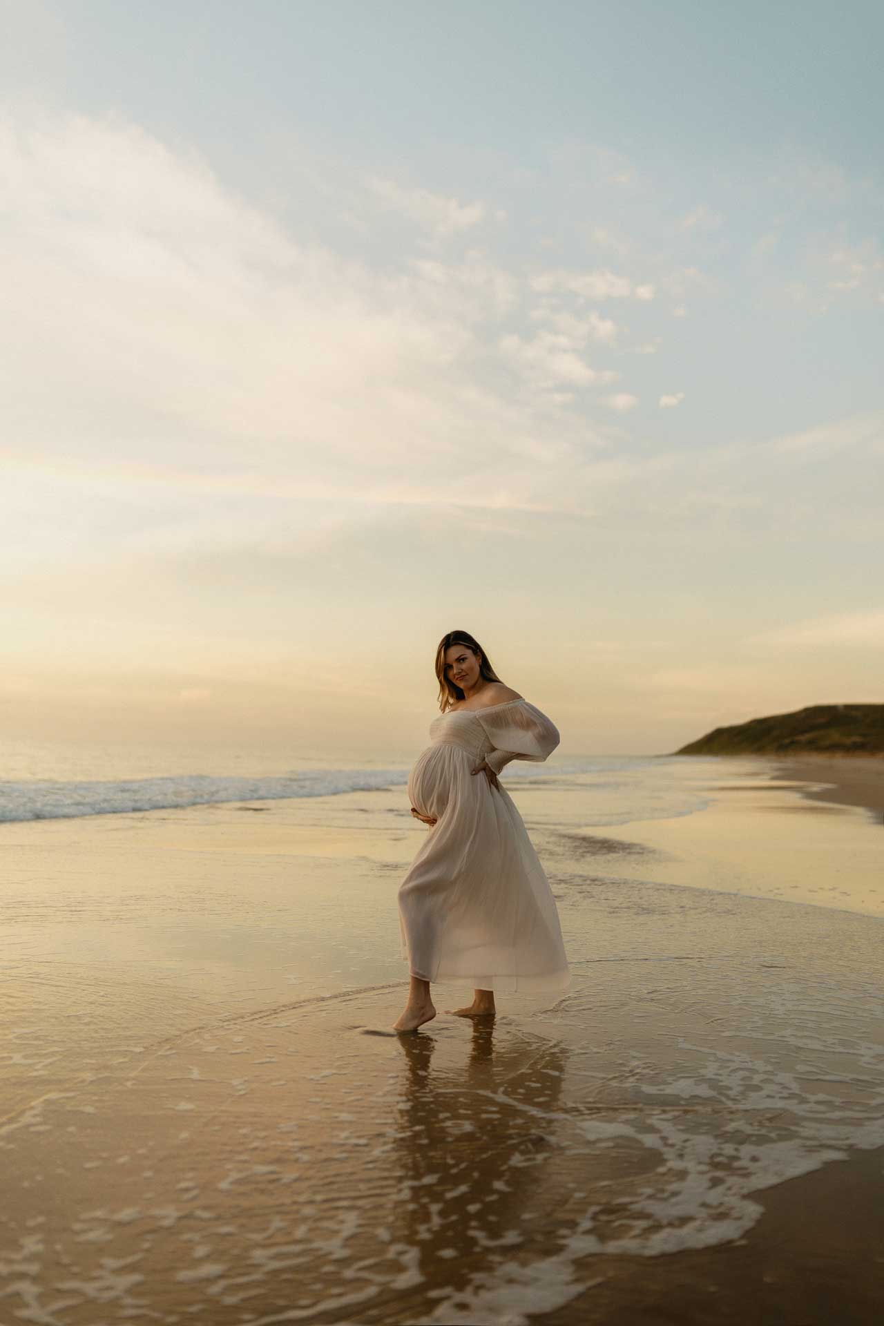 Pregnant woman standing in shallow water during a beach maternity session