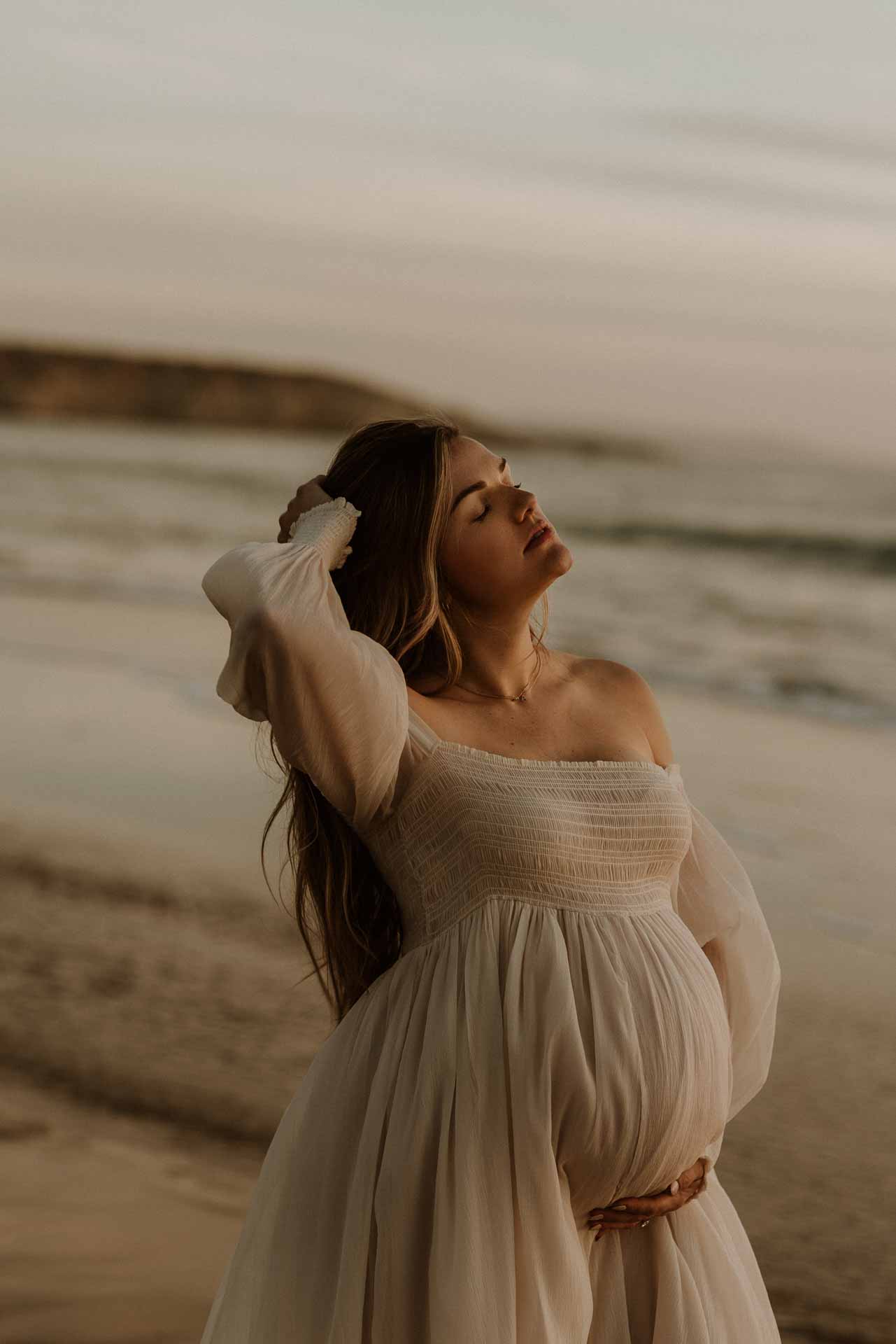 Pregnant woman posing beside the shoreline during a sunset maternity session