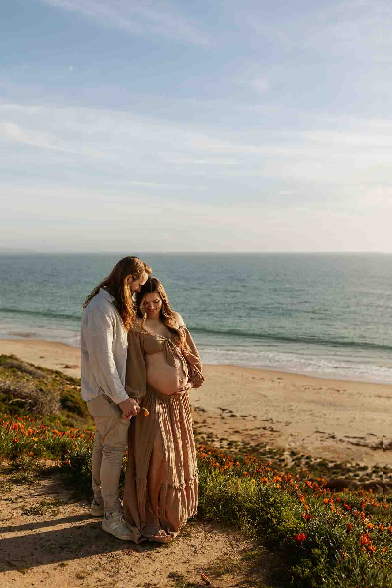Couple together during a coastal maternity session overlooking the beach