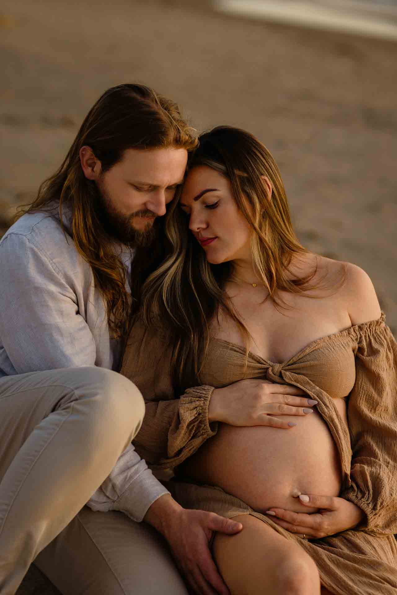 Couple sitting together on rocks during a beach maternity session