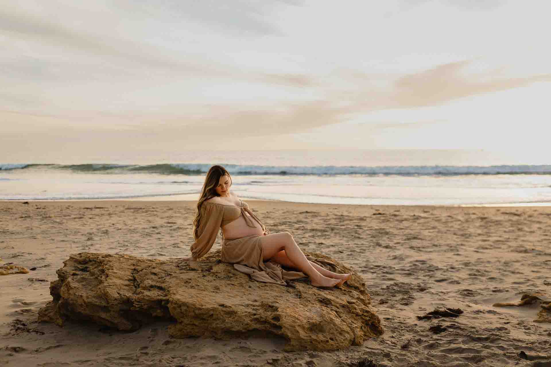 Pregnant woman sitting on rocks overlooking the ocean