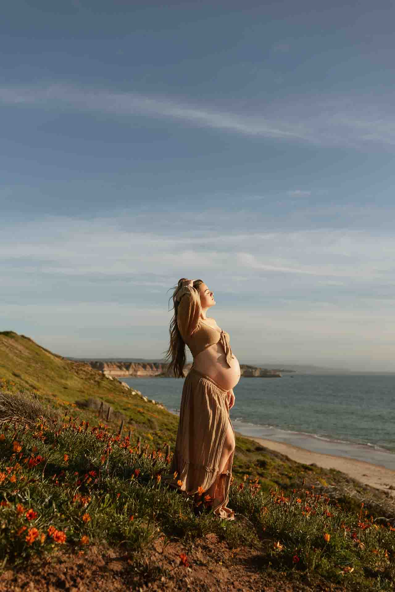 Pregnant woman standing among zinnias with the Adelaide coastline in the background