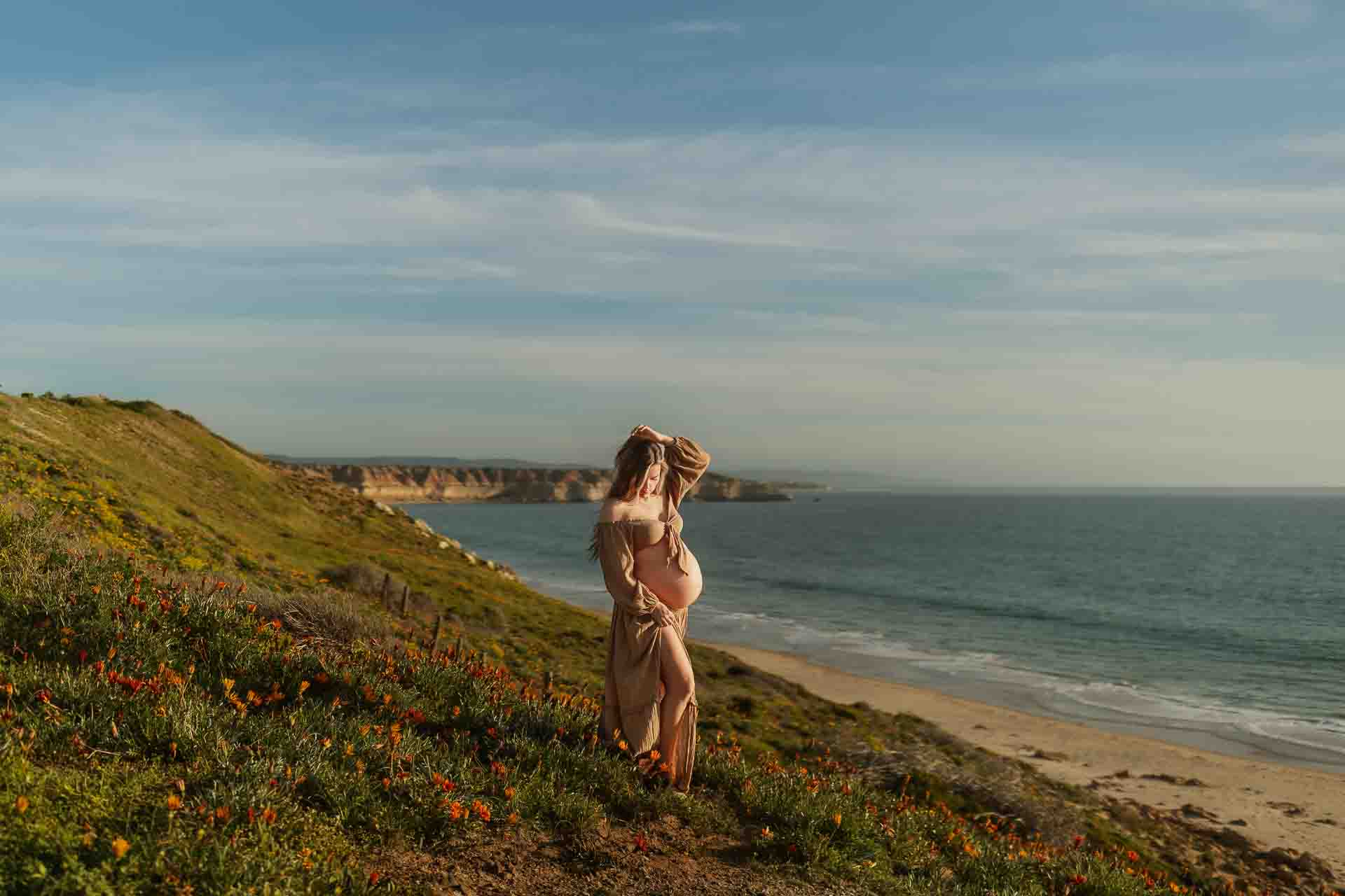 Pregnant woman standing among zinnias overlooking the ocean during a beach maternity session