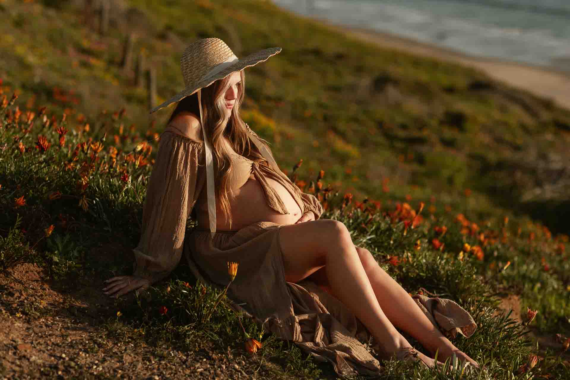 Pregnant woman sitting among zinnias overlooking the ocean during a beach maternity session